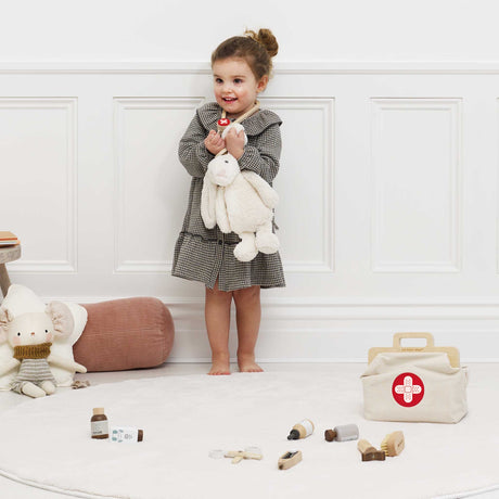 Little girl smiling while hugging a plush bunny and wearing a toy stethoscope near her vet kit.