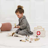 Young girl using toy wooden scissors on a plush mouse next to a vet play kit on a white rug.