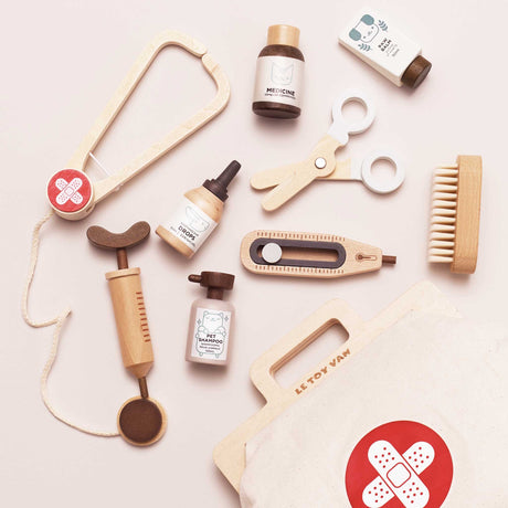 Flat lay of a wooden toy vet kit including a stethoscope, syringe, thermometer, scissors, brush, pet care medicine bottles, and a canvas medical bag.