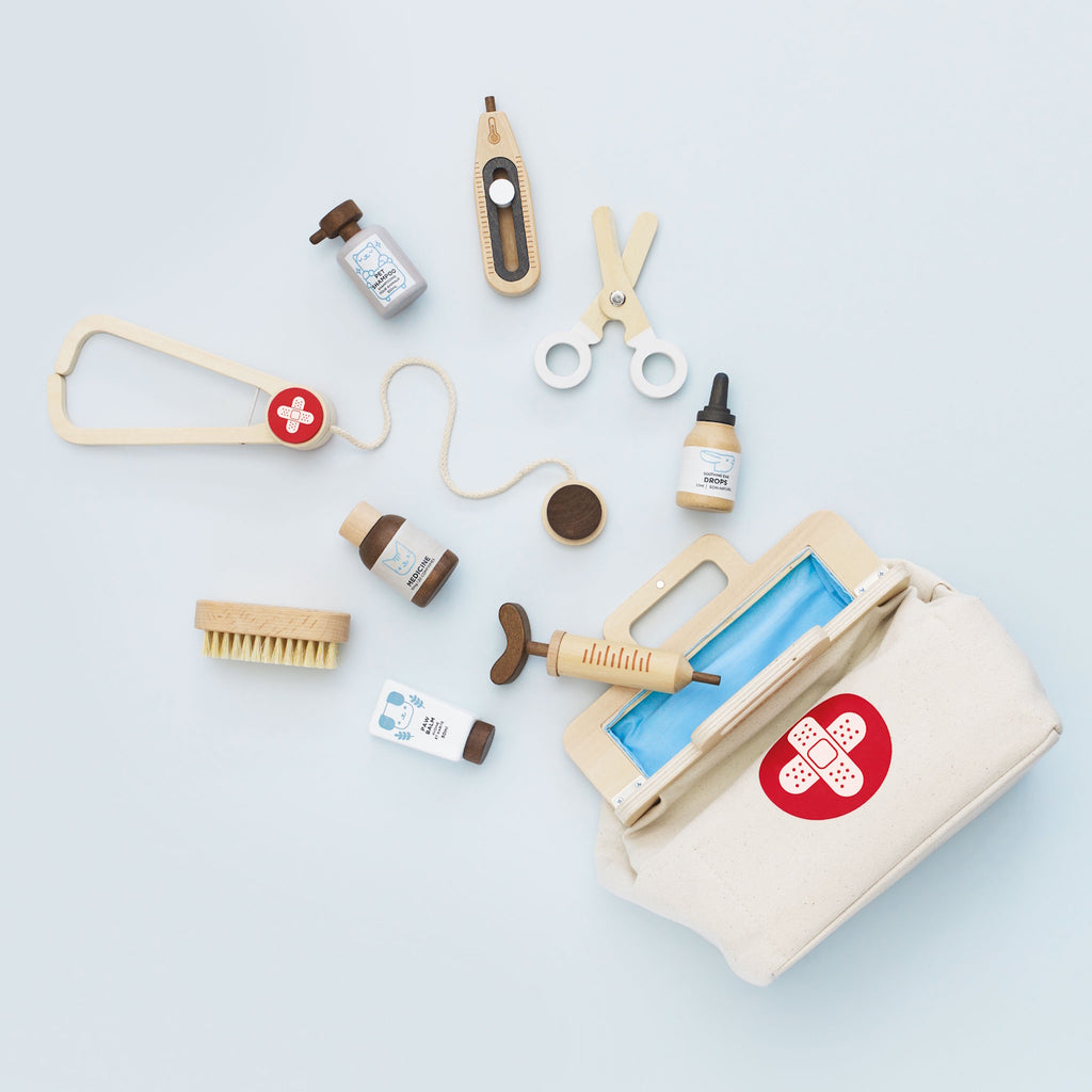 Toy veterinary kit featuring a fabric bag with a red cross, wooden syringe, scissors, brush, dropper, and bottles labeled medicine and pet shampoo. Playful tone.