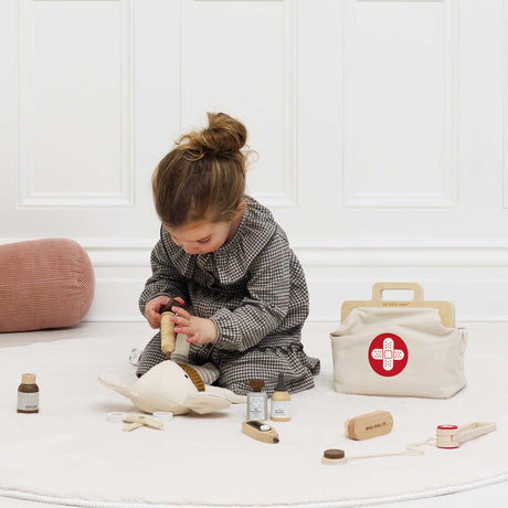Young girl using a wooden toy syringe on a plush mouse next to a vet medical bag.