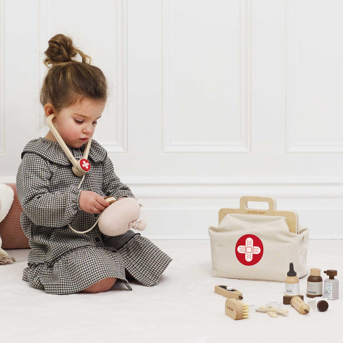 Little girl listening to a plush toy with a wooden stethoscope near her vet kit.