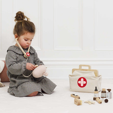 Little girl listening to a plush toy with a wooden stethoscope near her vet kit.