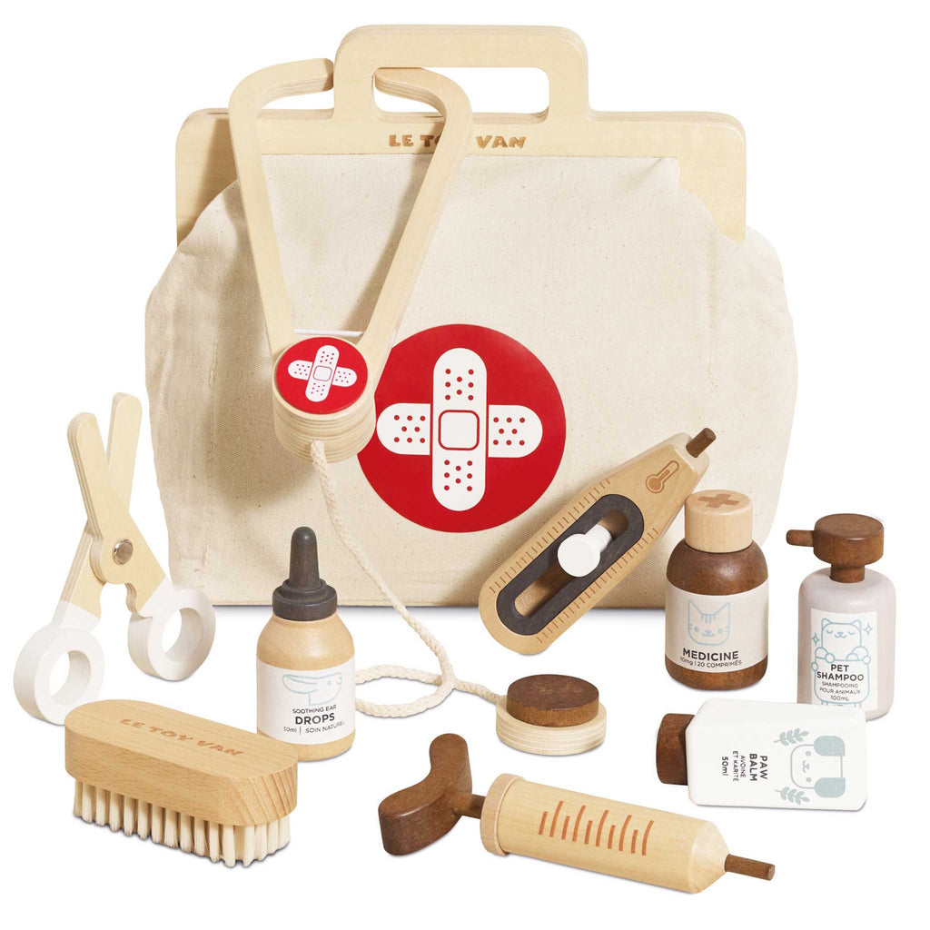 Toy veterinary kit featuring a fabric bag with a red cross, wooden syringe, scissors, brush, dropper, and bottles labeled medicine and pet shampoo. Playful tone.