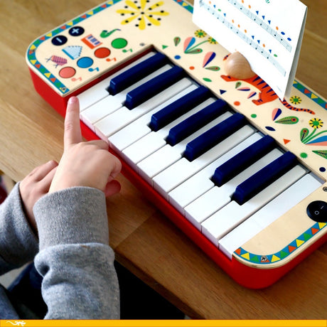 Djeco Animambo toy synthesiser with sheet music being played by a child's hand.