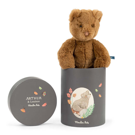 A fuzzy brown teddy bear sitting in a tall grey gift box decorated with illustrations of a bear and leaves.