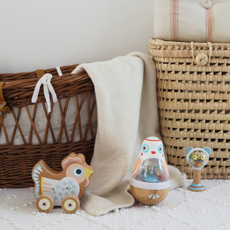 Wooden chicken pull toy and bird wobbler in a boho nursery with wicker baskets and cream baby blanket.