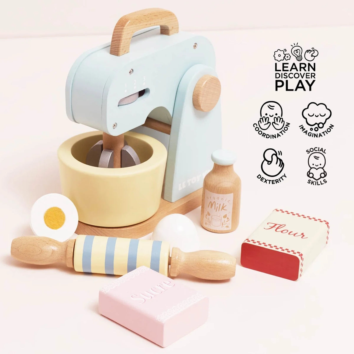 Wooden toy baking set with pastel blue mixer, bowl, rolling pin, milk bottle, egg halves, and flour/sugar boxes.