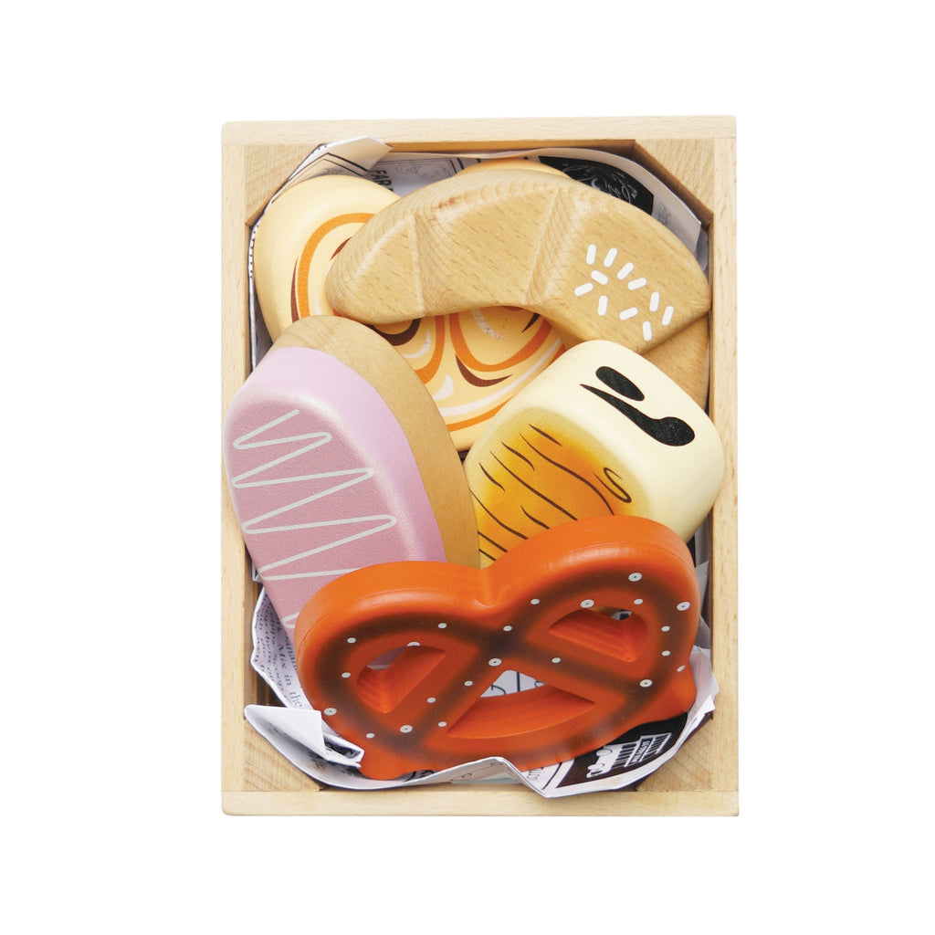 A wooden toy crate contains colorful, wooden bakery items, including a pretzel, croissant, and heart-shaped cookies, evoking a playful and cheerful mood.