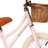 A charming vintage-inspired balance bike for kids, featuring a pastel pink frame, adjustable seat and handlebars, and a classic wicker basket.