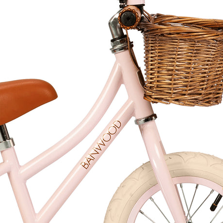 A charming vintage-inspired balance bike for kids, featuring a pastel pink frame, adjustable seat and handlebars, and a classic wicker basket.