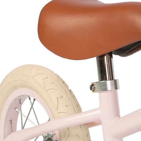 A charming vintage-inspired balance bike for kids, featuring a pastel pink frame, adjustable seat and handlebars, and a classic wicker basket.