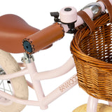 A charming vintage-inspired balance bike for kids, featuring a pastel pink frame, adjustable seat and handlebars, and a classic wicker basket.
