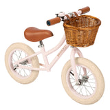 A charming vintage-inspired balance bike for kids, featuring a pastel pink frame, adjustable seat and handlebars, and a classic wicker basket.