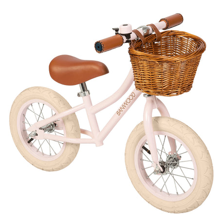 A charming vintage-inspired balance bike for kids, featuring a pastel pink frame, adjustable seat and handlebars, and a classic wicker basket.