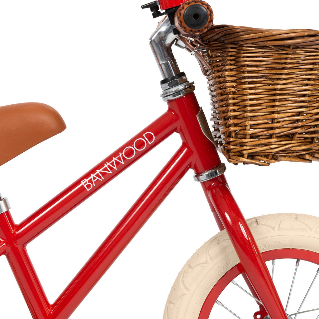 A vintage-style children’s balance bike featuring a bold red frame, adjustable seat and handlebars, and a timeless wicker basket.