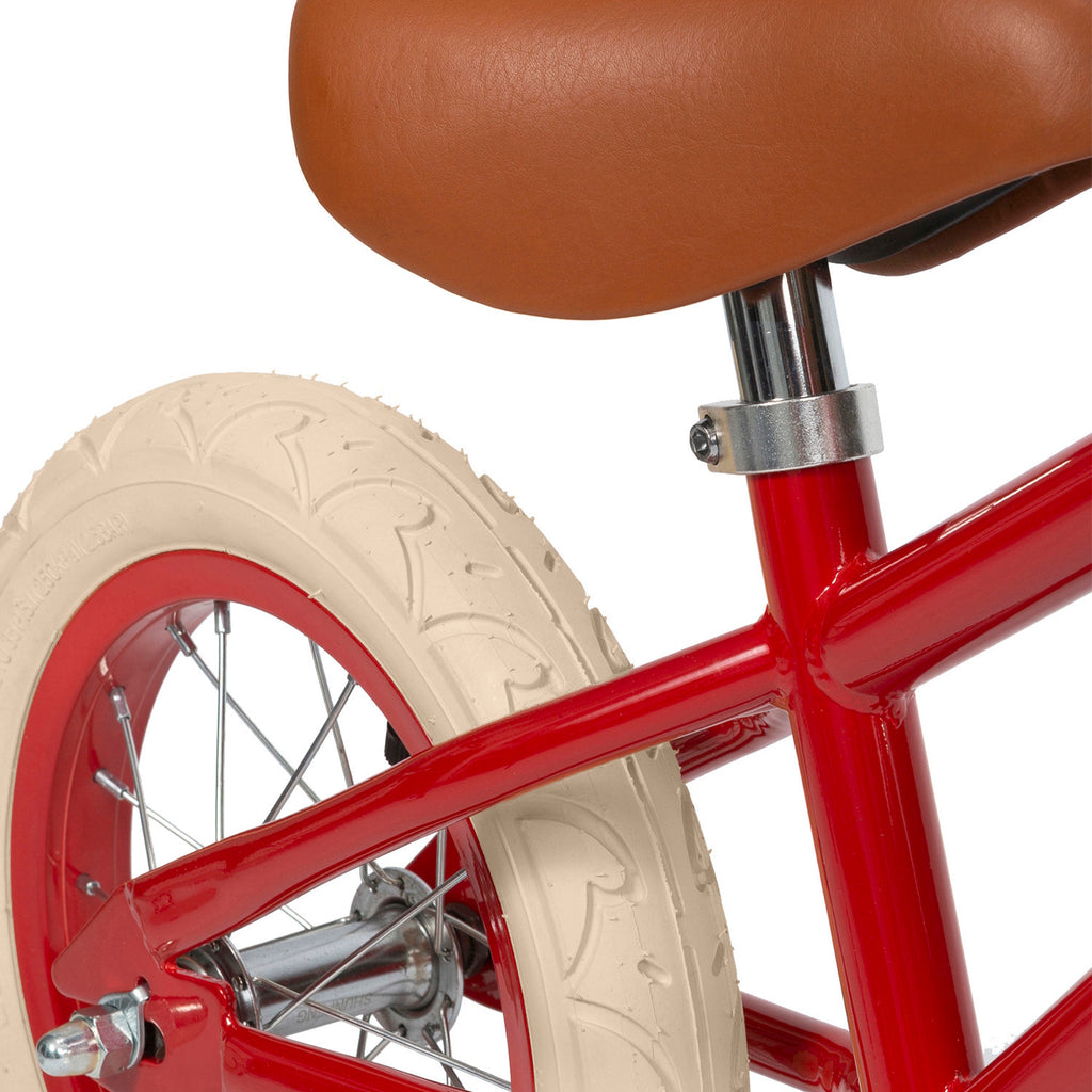 A vintage-style children’s balance bike featuring a bold red frame, adjustable seat and handlebars, and a timeless wicker basket.