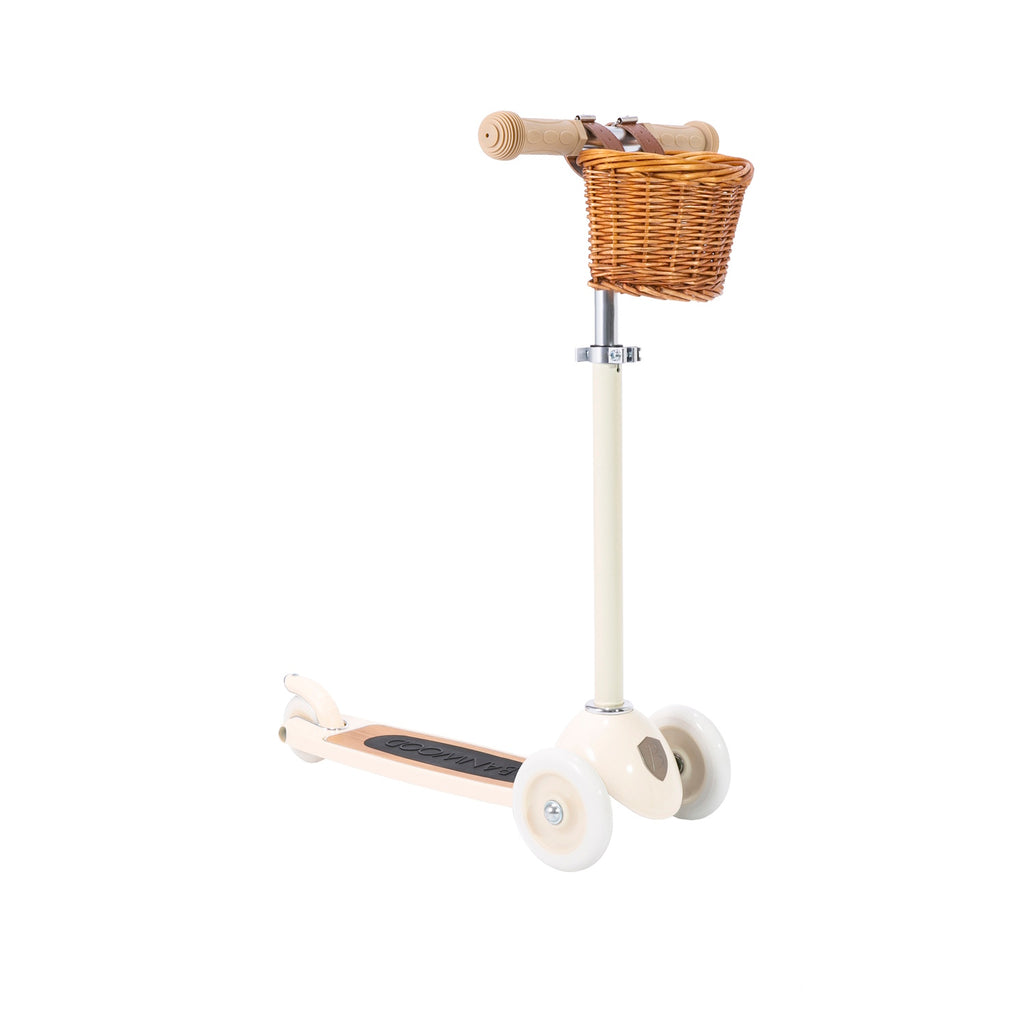 A stylish vintage-style kids' scooter in a soft cream color, featuring three wheels for stability, an adjustable handlebar, and a detachable wicker basket.