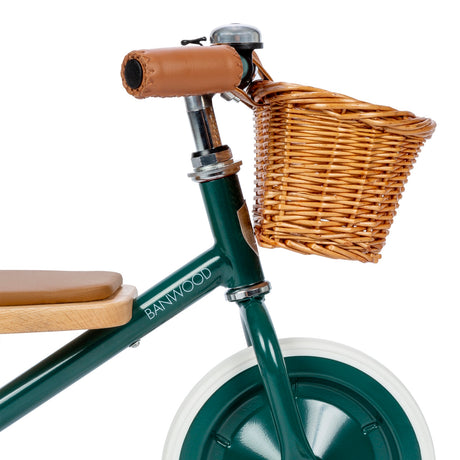 Close-up of Banwood green tricycle handlebars with brown leather grips, bell, and wicker basket.