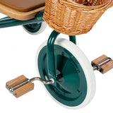 Close-up of Banwood green tricycle front wheel with wooden pedals, white tire, and wicker basket.