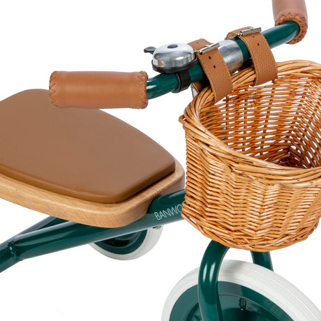 Close-up view of Banwood green tricycle seat, bell, handlebars, and wicker basket.