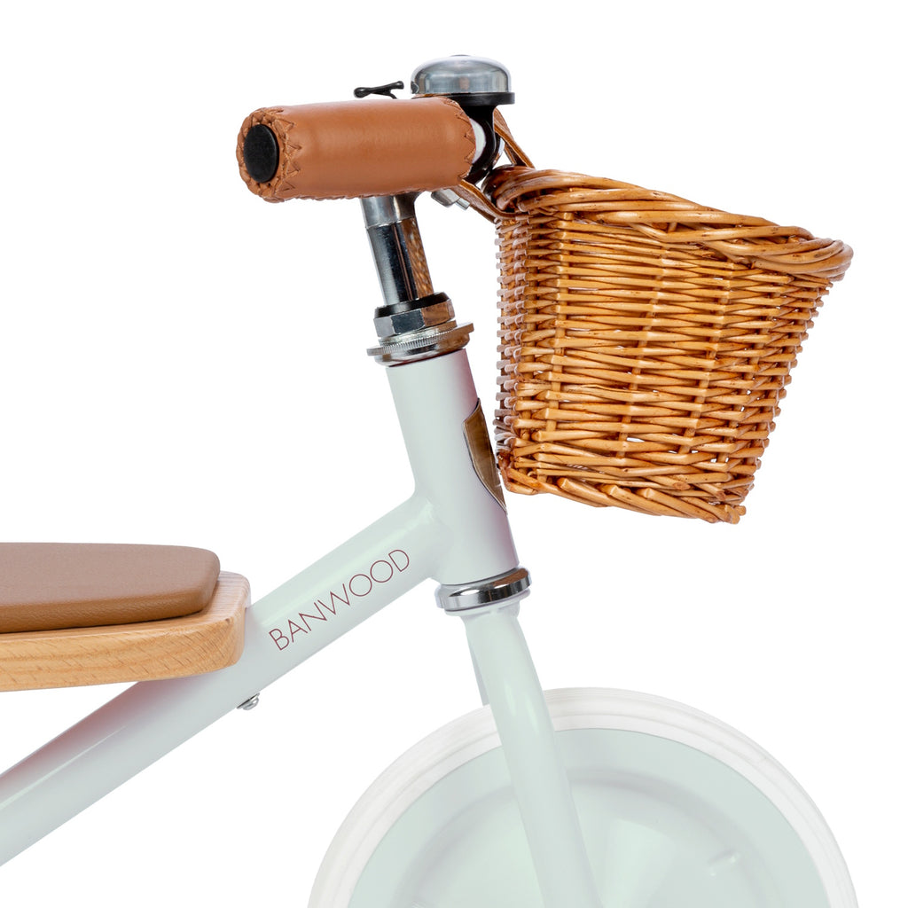 A vintage-inspired children's tricycle in a soft mint green, featuring a sturdy steel frame, wooden pedals, a removable push bar, and a wicker basket.