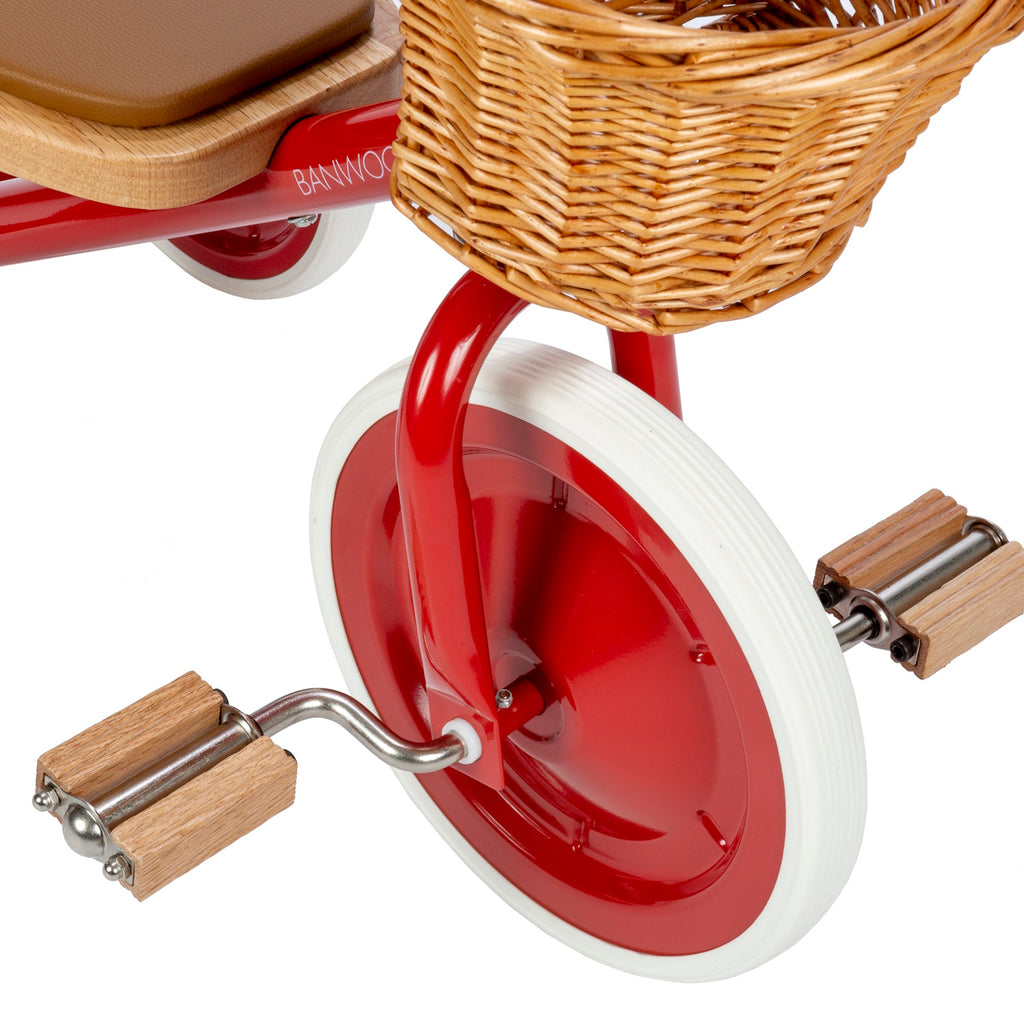 A classic children’s tricycle with a vibrant red steel frame, wooden pedals, removable push bar, and a wicker basket for timeless style and fun rides.