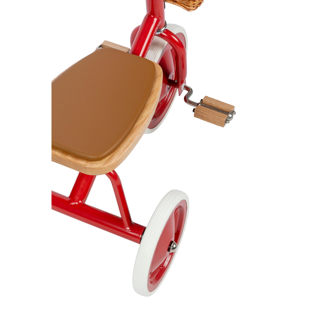 A classic children’s tricycle with a vibrant red steel frame, wooden pedals, removable push bar, and a wicker basket for timeless style and fun rides.
