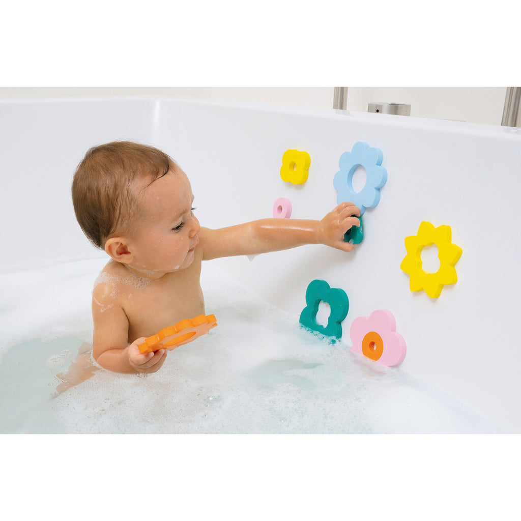 A baby in a bathtub plays with colorful foam flower toys on the wall. The bath is filled with bubbles, and the mood is playful and cheerful.