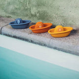 Three colorful toy boats with animal faces lined up on the edge of a pool.