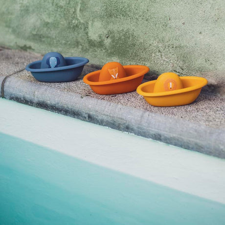 Three colorful toy boats with animal faces lined up on the edge of a pool.
