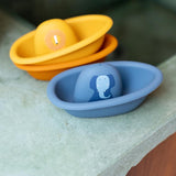 A blue toy boat with an elephant print next to stacked yellow and orange toy boats on a ledge.