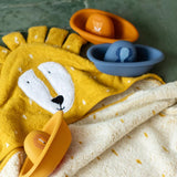 Three colorful toy boats with animal designs resting on a yellow lion-themed hooded towel.