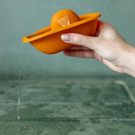 A hand holding an orange silicone fox bath toy boat as water pours out of its spout.