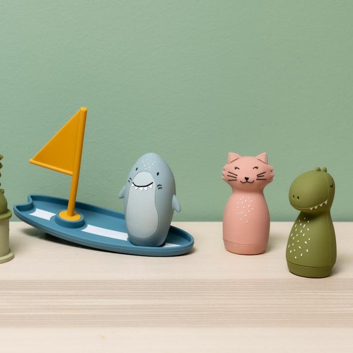 Shark bath toy on surfboard with cat and dinosaur figures on a wooden shelf.
