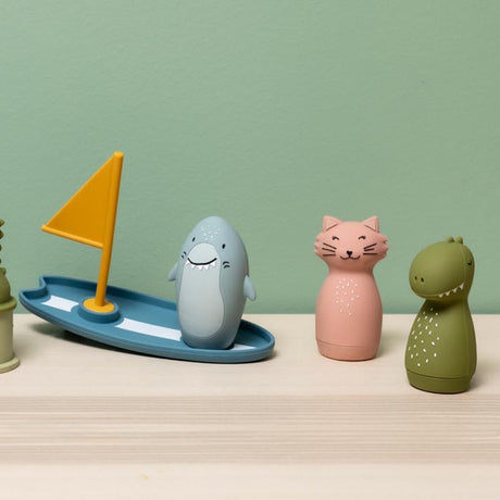 Shark bath toy on surfboard with cat and dinosaur figures on a wooden shelf.