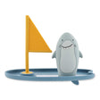 Friendly shark bath toy standing on a blue surfboard with a yellow sail on a white background.