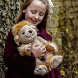 Young girl wearing a maroon coat smiling as she cradles a plush beige creature toy with fluffy yellow hair.