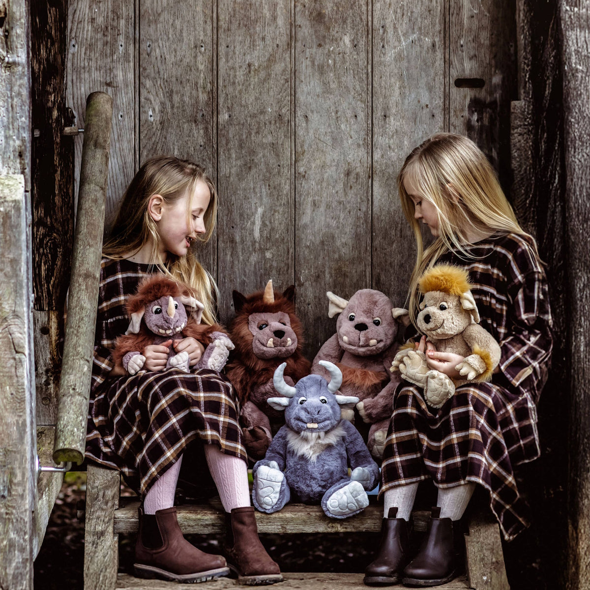Two young girls sitting on wooden steps outdoors surrounded by a variety of plush creature toys.
