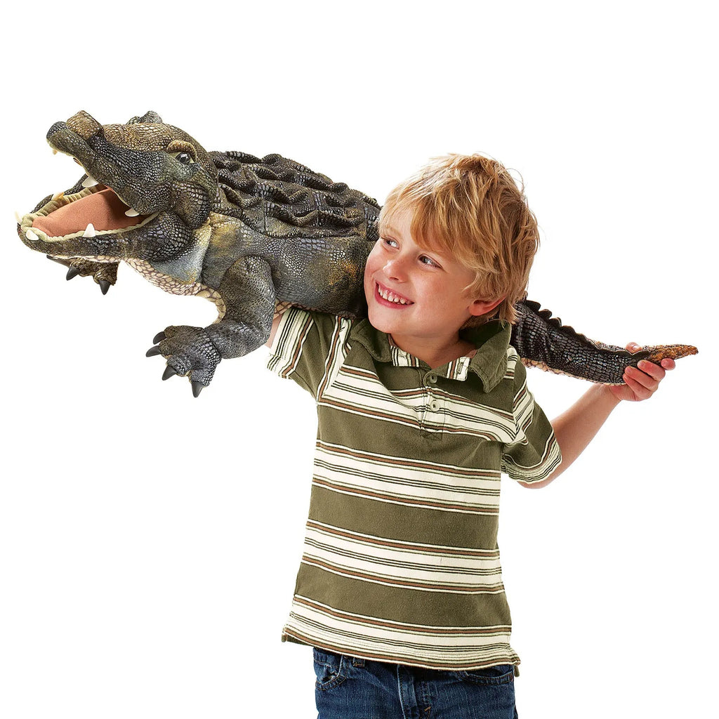 A smiling child in a striped shirt holds a large toy crocodile on their shoulder, conveying playfulness and joy. The crocodile's mouth is open.