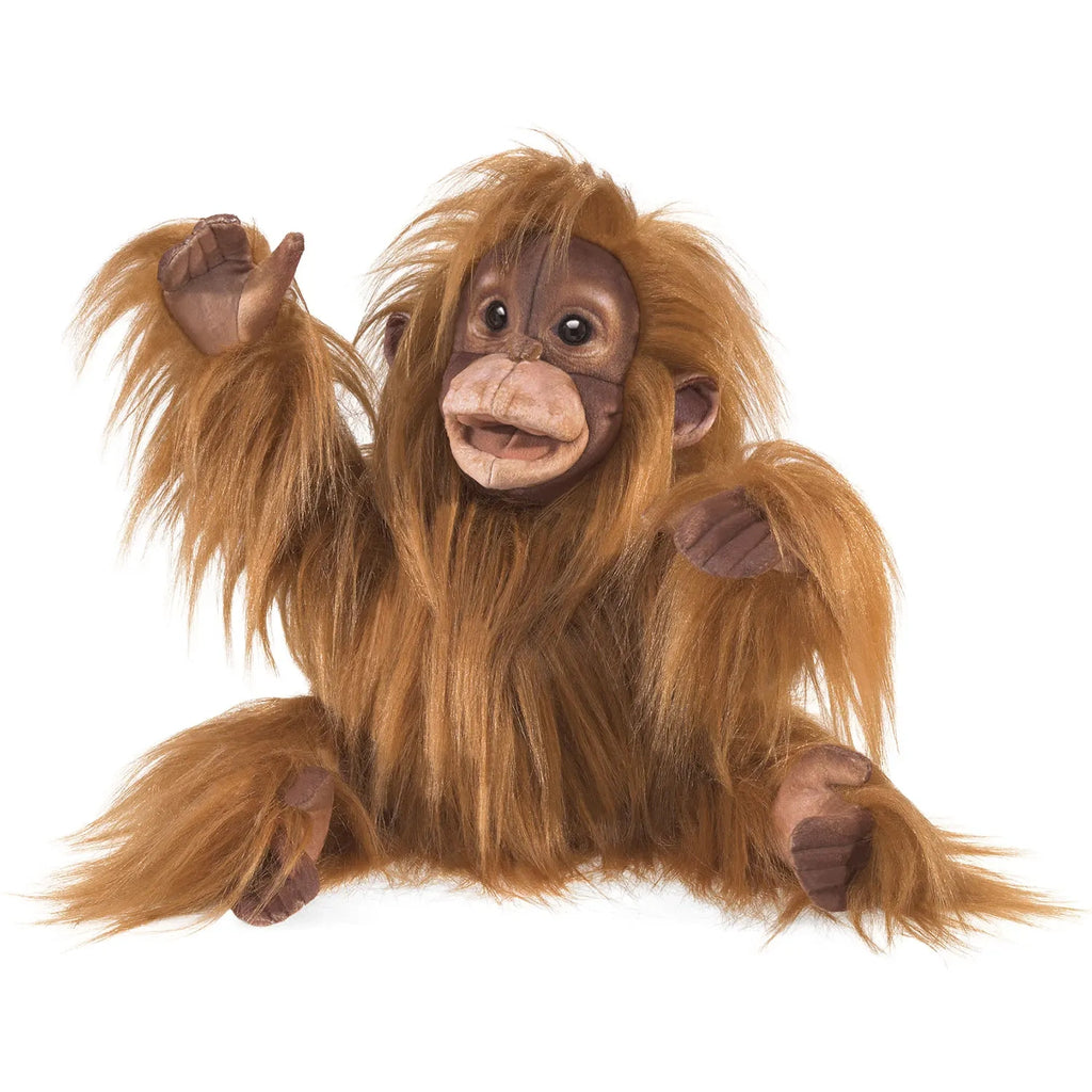 A plush orangutan toy with long, shaggy orange-brown fur sits upright, raising one arm. It has a friendly expression and detailed facial features.