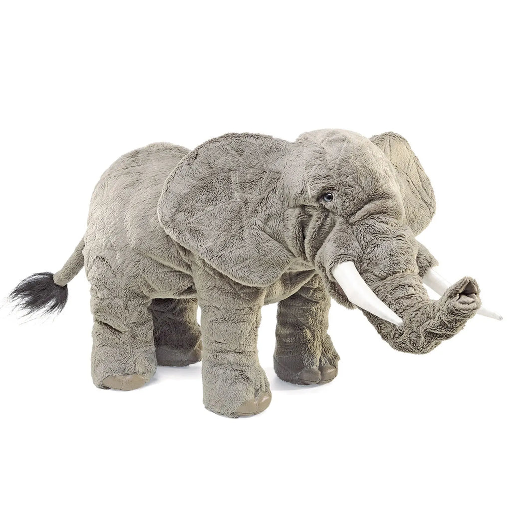 A large, realistic gray plush elephant standing on a white background. It has detailed features like tusks and a trunk, conveying a lifelike appearance.
