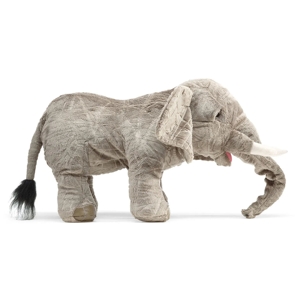 A large, realistic gray plush elephant standing on a white background. It has detailed features like tusks and a trunk, conveying a lifelike appearance.