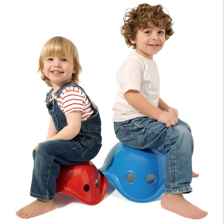 Two smiling young children sitting back-to-back on red and blue Bilibo seat toys against a white background.