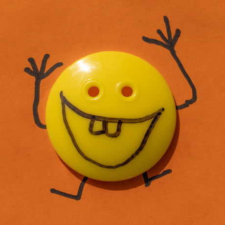 A quirky image of a yellow button face with hand-drawn marker limbs and buck teeth, against a bright orange background.