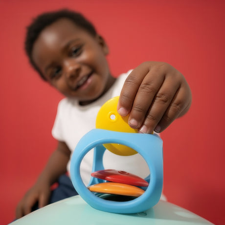 A smiling child inserts a yellow Bilibo Game Node into a blue Oibo elastic toy against a vibrant red background.