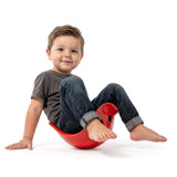 Toddler boy smiling and playing in a red Bilibo seat, developing balance and motor skills on a white background.