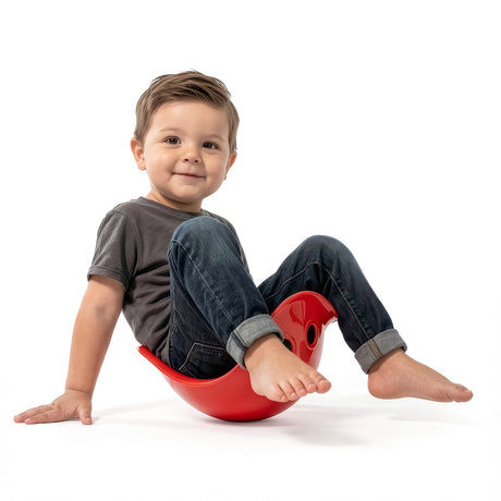 Toddler boy smiling and playing in a red Bilibo seat, developing balance and motor skills on a white background.