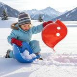 Toddler playing in snow with red and blue Bilibo shells, scooping snowballs in a scenic winter mountain landscape.