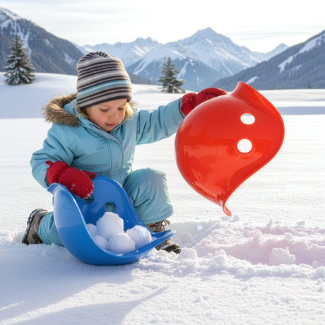 Toddler playing in snow with red and blue Bilibo shells, scooping snowballs in a scenic winter mountain landscape.